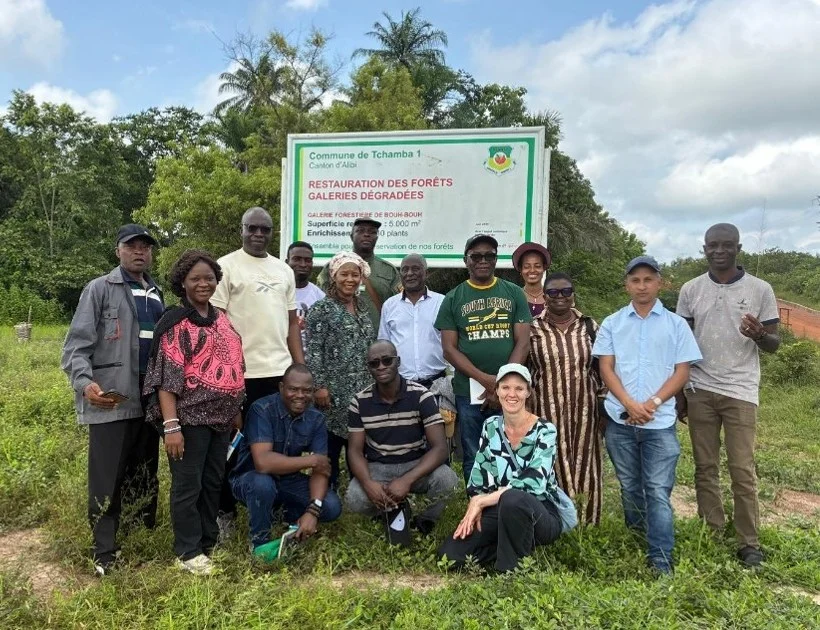 ASCEND researchers and community members gathered in front of a forest restoration sign in Tchamba